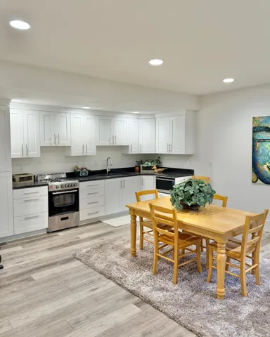 Kitchen with stainless steel range with gas stovetop, white cabinetry, dark countertops, light wood finished floors, and recessed lighting