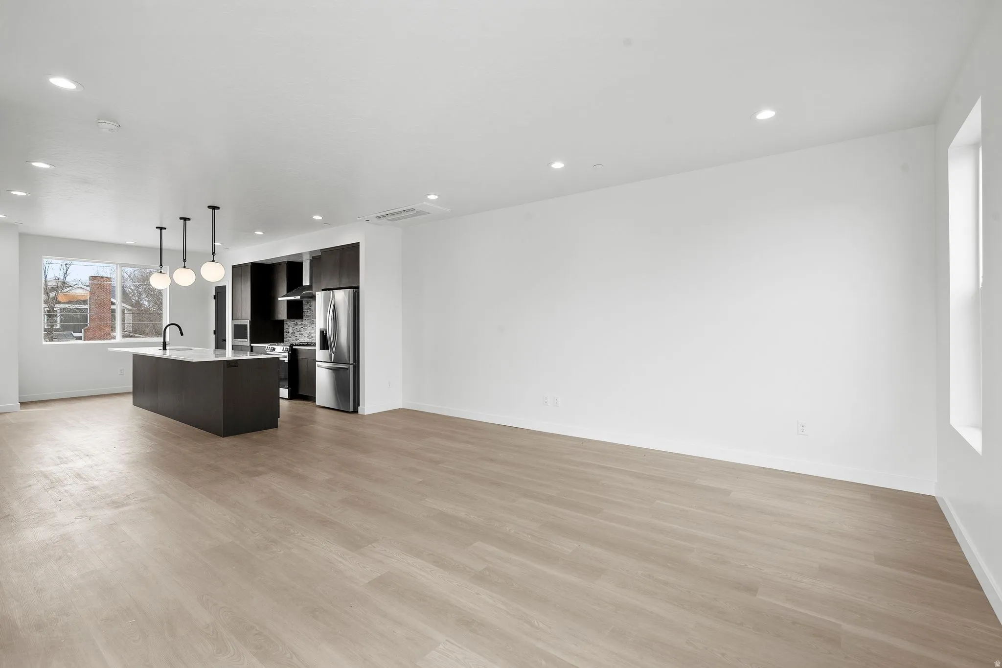 Kitchen with open floor plan, an island with sink, stainless steel appliances, hanging light fixtures, and light wood-style floors