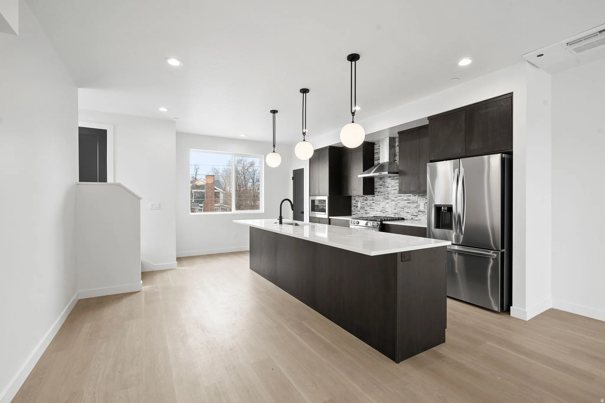 Kitchen with dark wood finish cabinets, stainless steel appliances, a kitchen island with sink, light stone counters, and light wood-style flooring