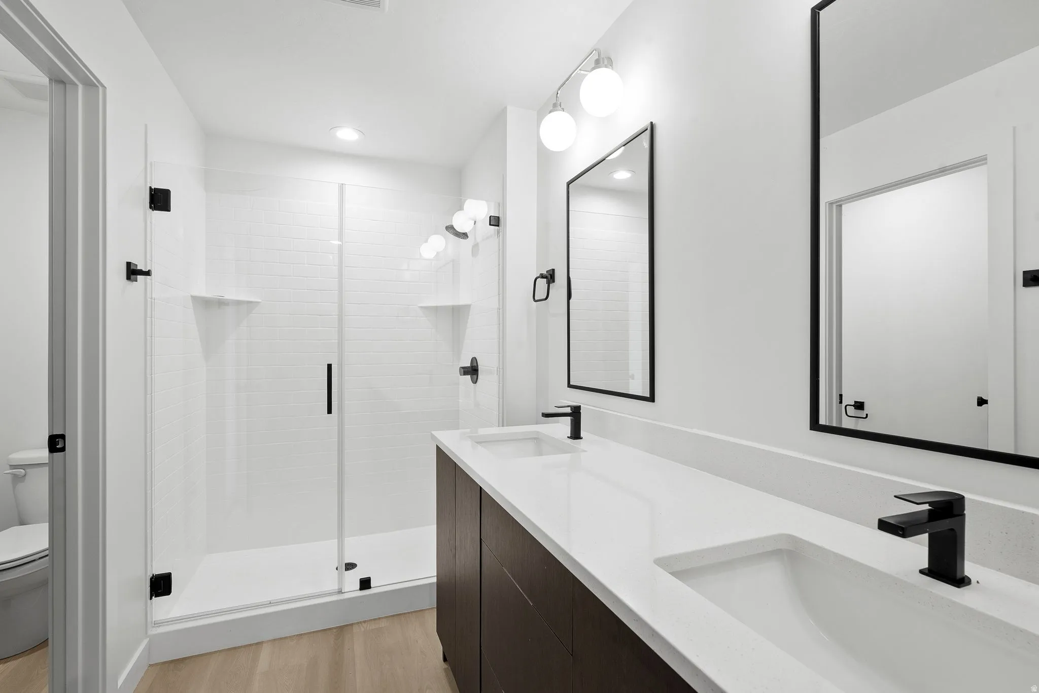 Bathroom featuring double vanity, a shower stall, light wood-style flooring, and recessed lighting