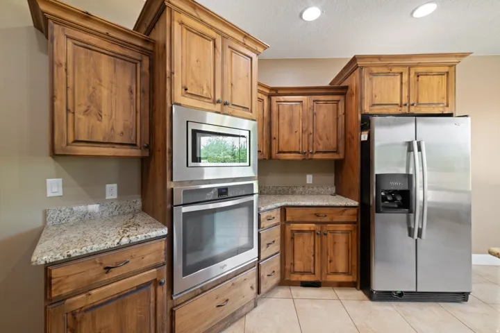 Kitchen with stainless steel appliances, light stone countertops, wood finish cabinetry, a textured ceiling, and light tile patterned floors