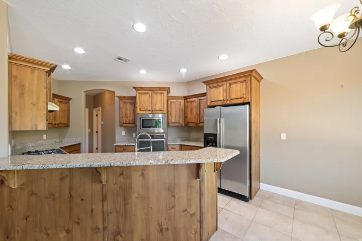 Kitchen featuring wood finish cabinets, stainless steel appliances, a peninsula, a kitchen breakfast bar, and light stone counters