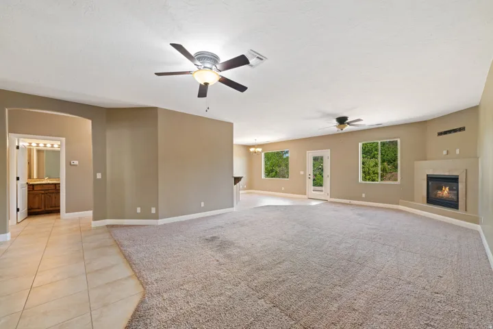 Unfurnished living room featuring a glass covered fireplace, ceiling fan, arched walkways, and light carpet