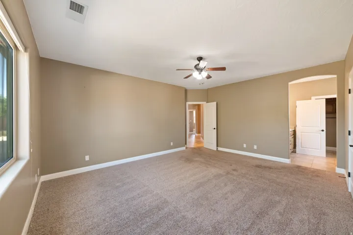 Master bedroom with light colored carpet, arched walkways, ceiling fan, and ensuite bathroom