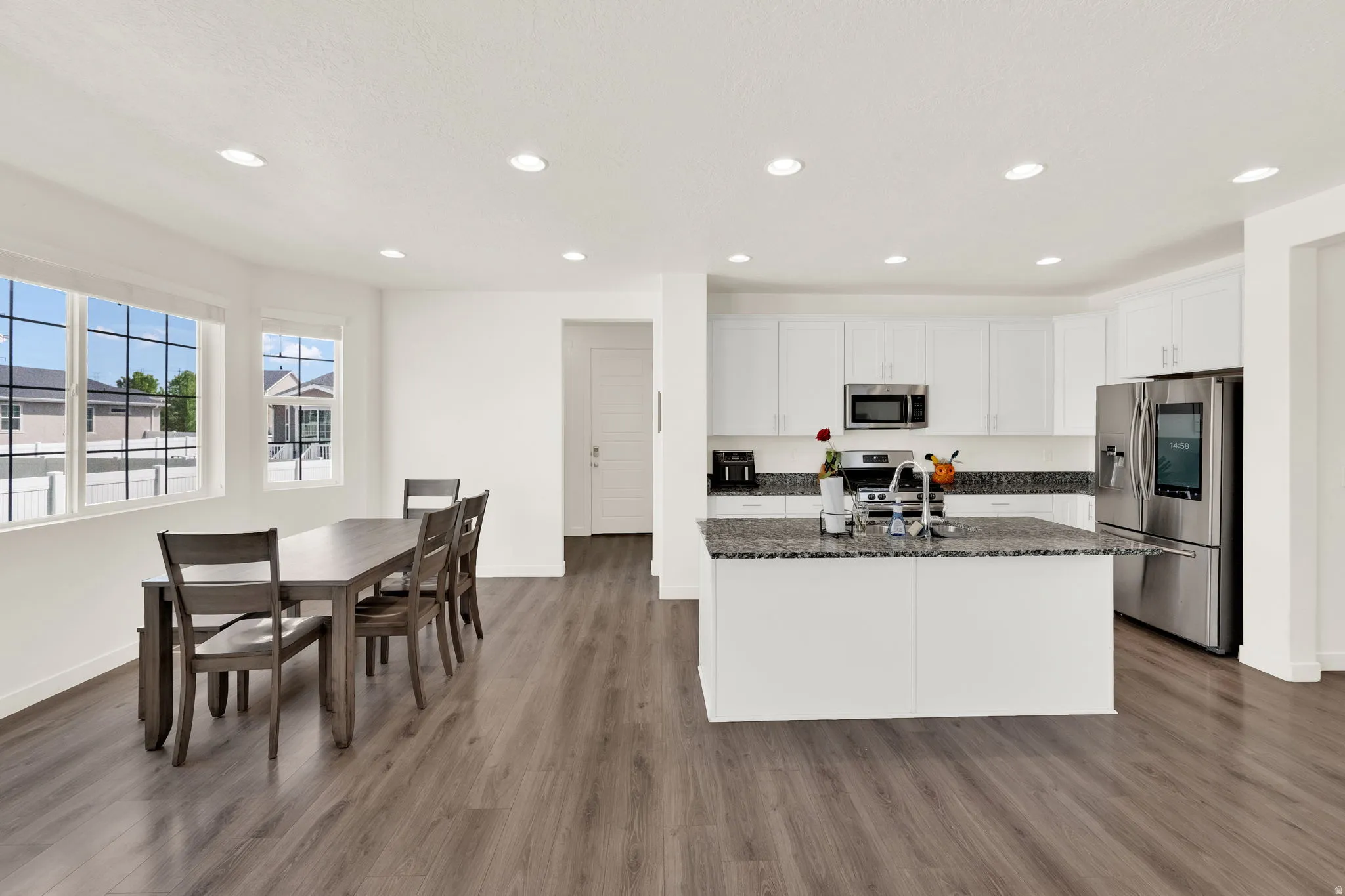 Kitchen with stainless steel appliances, dark stone countertops, white cabinetry, a kitchen island with sink, and recessed lighting