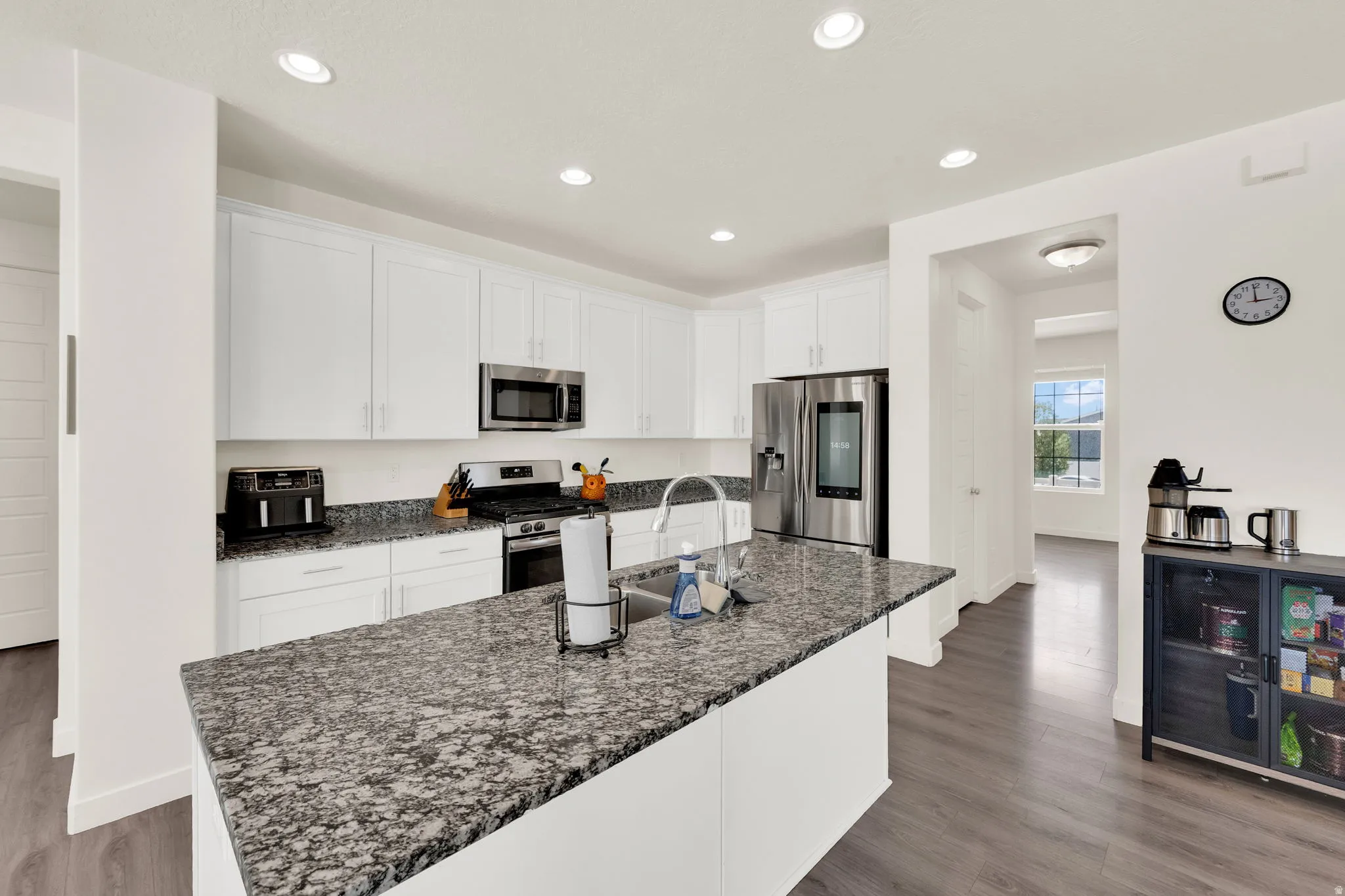 Kitchen featuring white cabinets, stainless steel appliances, a kitchen island with sink, dark stone counters, and dark wood-type flooring