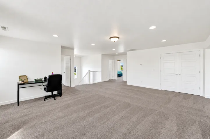 Expansive carpeted area with white walls, recessed lighting, and a semi-flush mount fixture