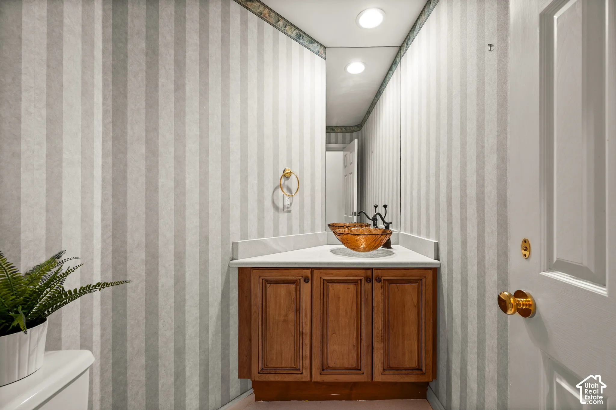 Corner vanity featuring a vessel sink with a dark bronze faucet, a white countertop, and wood-finish cabinetry