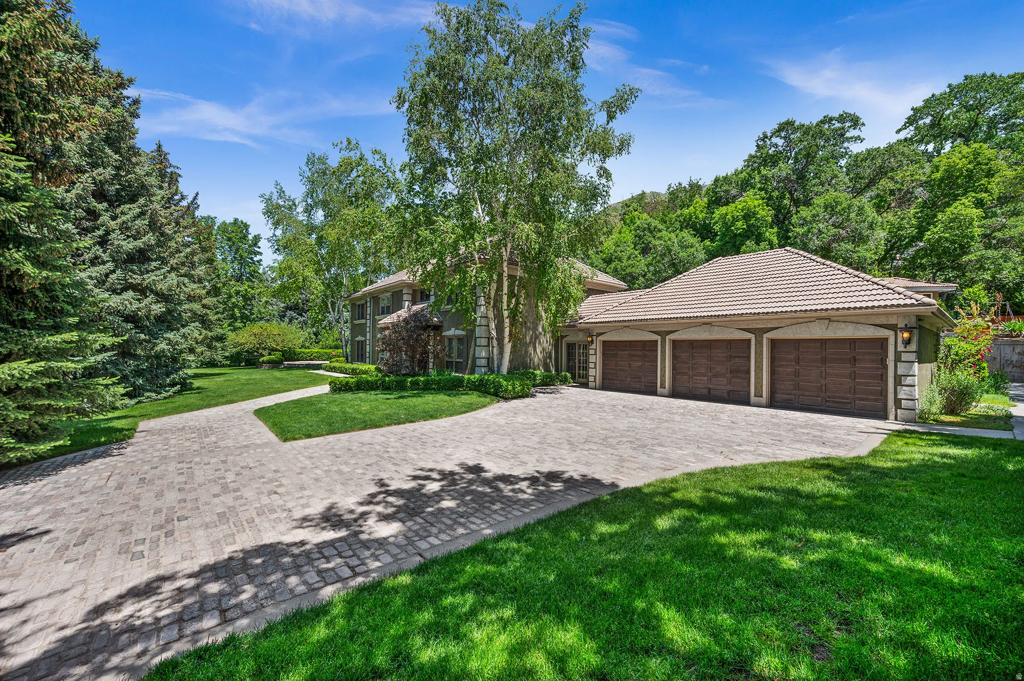 View of front of house with a tiled roof, a front yard, decorative driveway, and attached  3-car garage