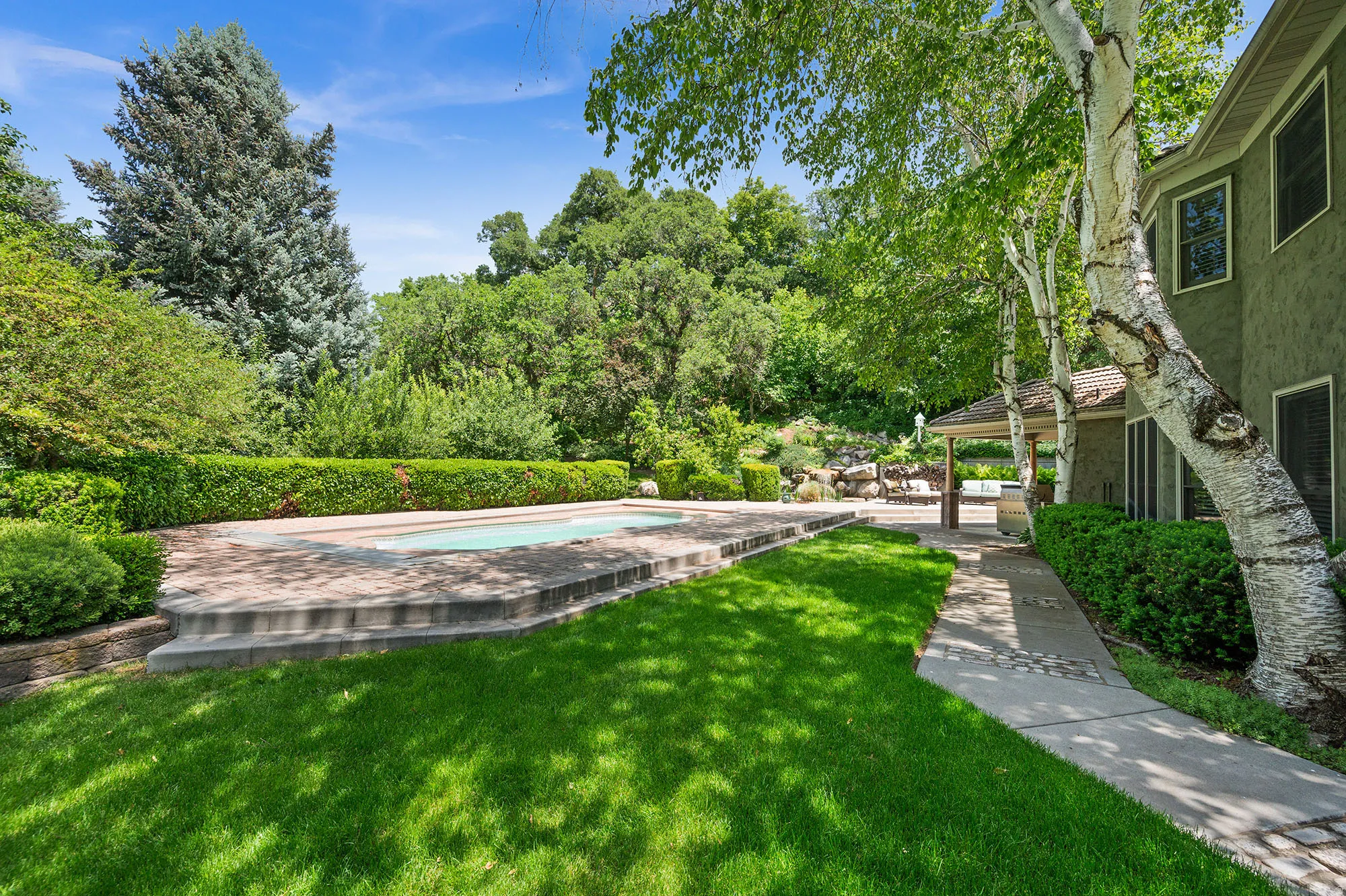 View of green lawn with an outdoor pool, view of wooded area, and a patio