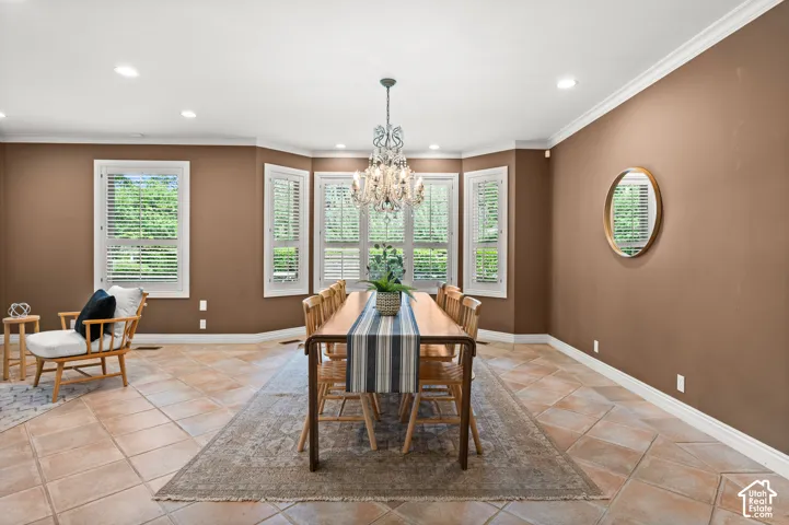 Dining space featuring multiple windows with plantation shutters, a chandelier light fixture, recessed lighting, crown molding, and tile flooring