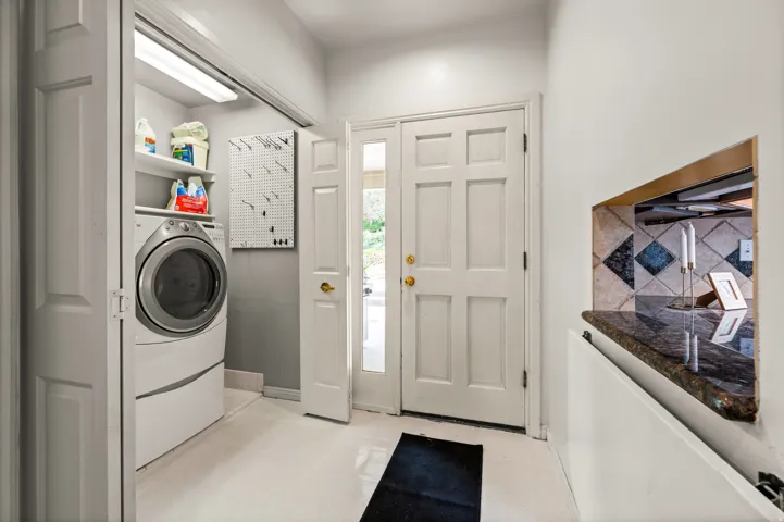 Practical utility space featuring a laundry closet with shelving, a built-in pass-through with a stone countertop, and light-toned flooring