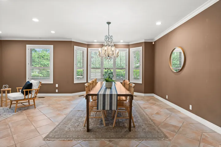 Dining space featuring multiple windows with plantation shutters, a chandelier light fixture, recessed lighting, crown molding, and tile flooring