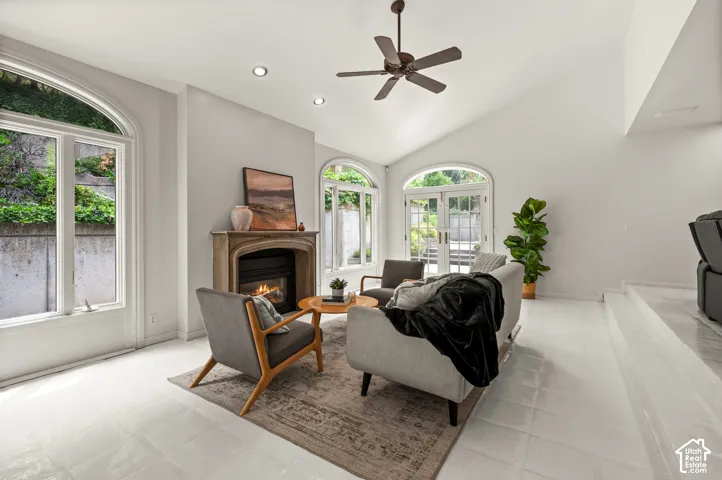 Bright living space with vaulted ceilings, a stone fireplace, arched windows, recessed lighting, and light-toned flooring with 2 patio doors.