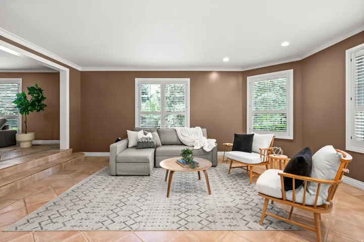 Spacious living area featuring large windows with white louvered blinds, recessed ceiling lighting, crown molding, and tiled flooring