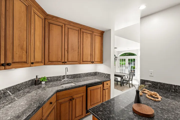 Bar area featuring granite countertops, wood cabinetry with black hardware, a stainless steel sink.