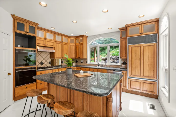 Kitchen featuring a central island with a stone countertop, extensive wood cabinetry, built-in double ovens, and an integrated panel-ready refrigerator