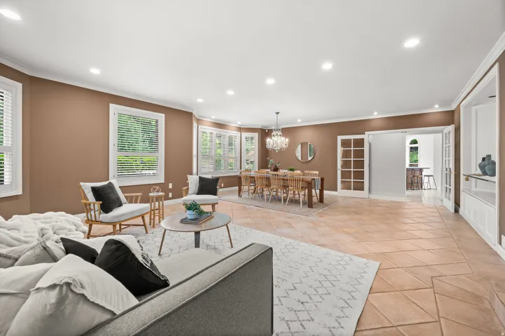Spacious interior featuring a combination of tile flooring and an area rug, built-in shelving, recessed lighting, and multiple windows with white plantation shutters.