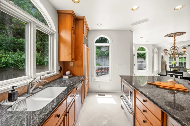 Kitchen featuring wood cabinetry, granite countertops, white tile flooring.