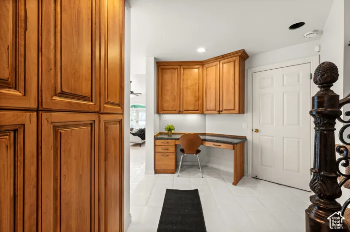 Built-in desk area featuring wood-finish cabinetry, dark stone-finish countertop, and more storage or pantry space.