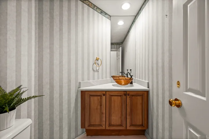Corner vanity featuring a vessel sink with a dark bronze faucet, a white countertop, and wood-finish cabinetry
