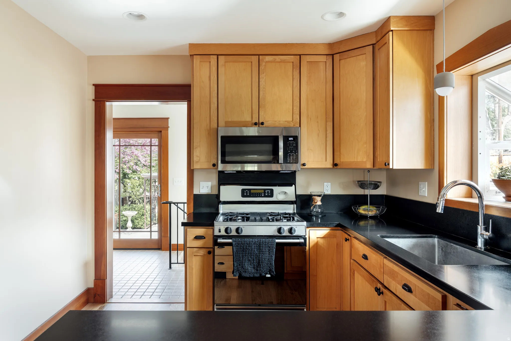 Kitchen with gas stove, dark countertops, stainless steel microwave, wood finish cabinets, and plenty of natural light