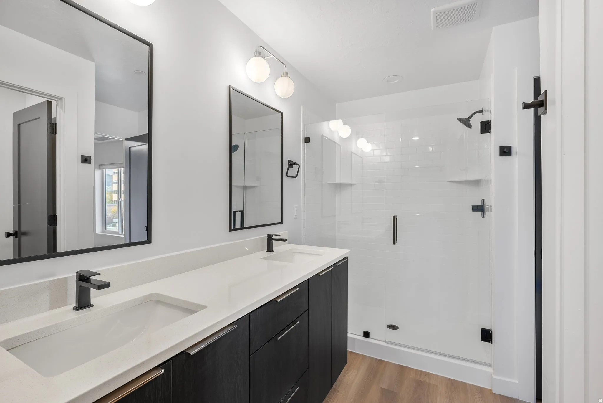 Photos are of a finished unit - Full bath featuring double vanity, a shower stall, and light wood-style floors