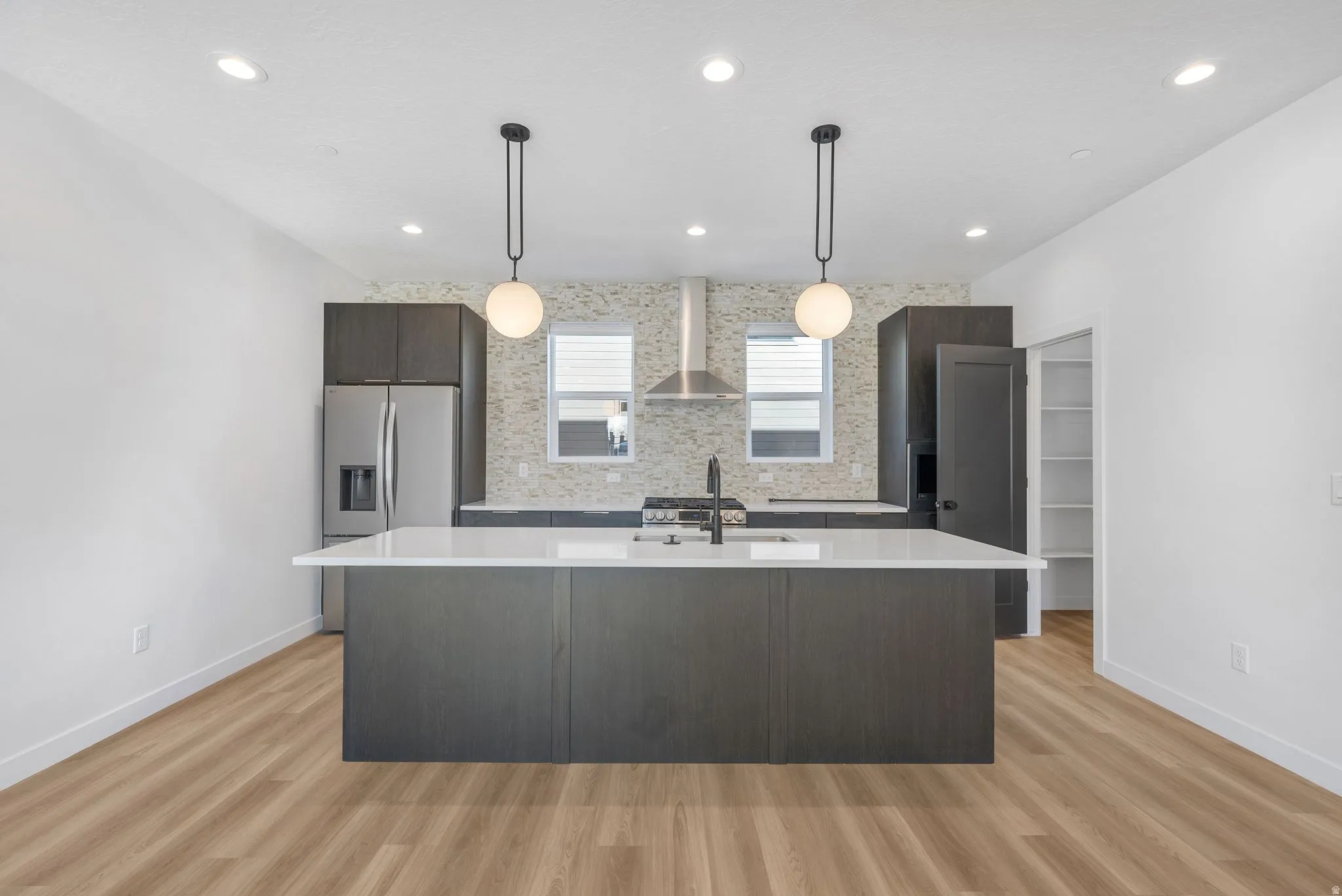 Photos are of a finished unit - Kitchen featuring dark wood finish cabinets, stainless steel fridge, light wood finished floors, decorative light fixtures, and a center island with sink