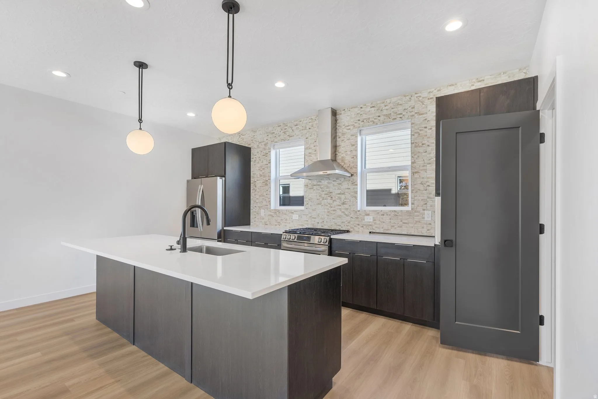 Photos are of a finished unit - Kitchen featuring light wood-style floors, dark wood finish cabinetry, pendant lighting, stainless steel appliances, and an island with sink