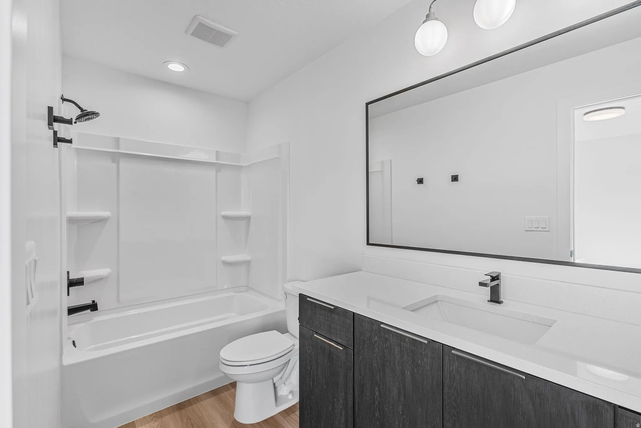 Photos are of a finished unit - Full bathroom with vanity, light wood finished floors, and washtub / shower combination