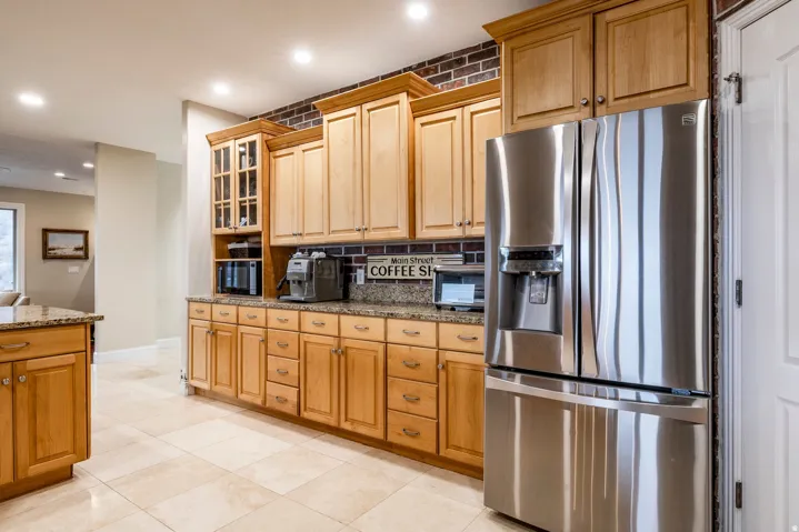Kitchen featuring stainless steel fridge with ice dispenser, recessed lighting, dark stone counters, glass insert cabinets, and black microwave