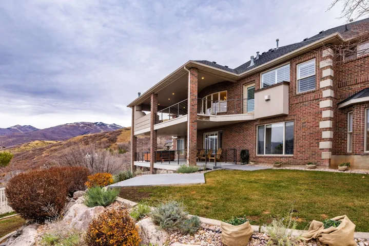 Rear view of property featuring a patio, brick siding, a balcony, a mountain view, and a yard