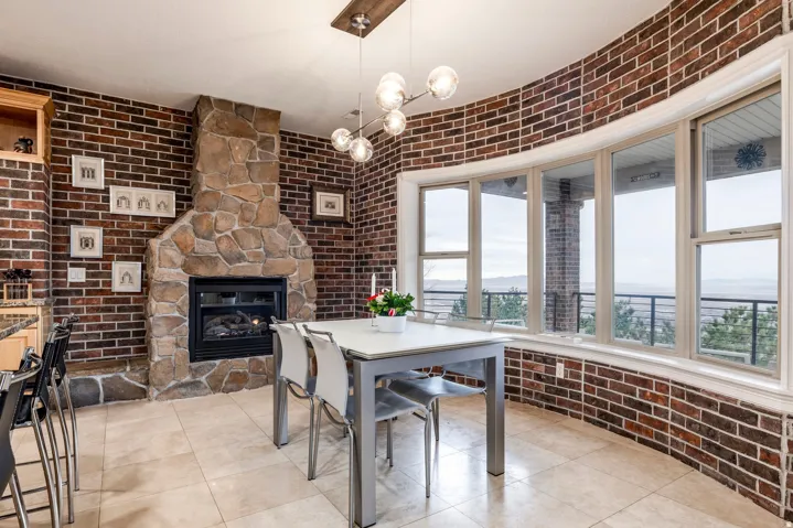 Dining room featuring brick wall, a chandelier, a stone fireplace, and light tile patterned flooring