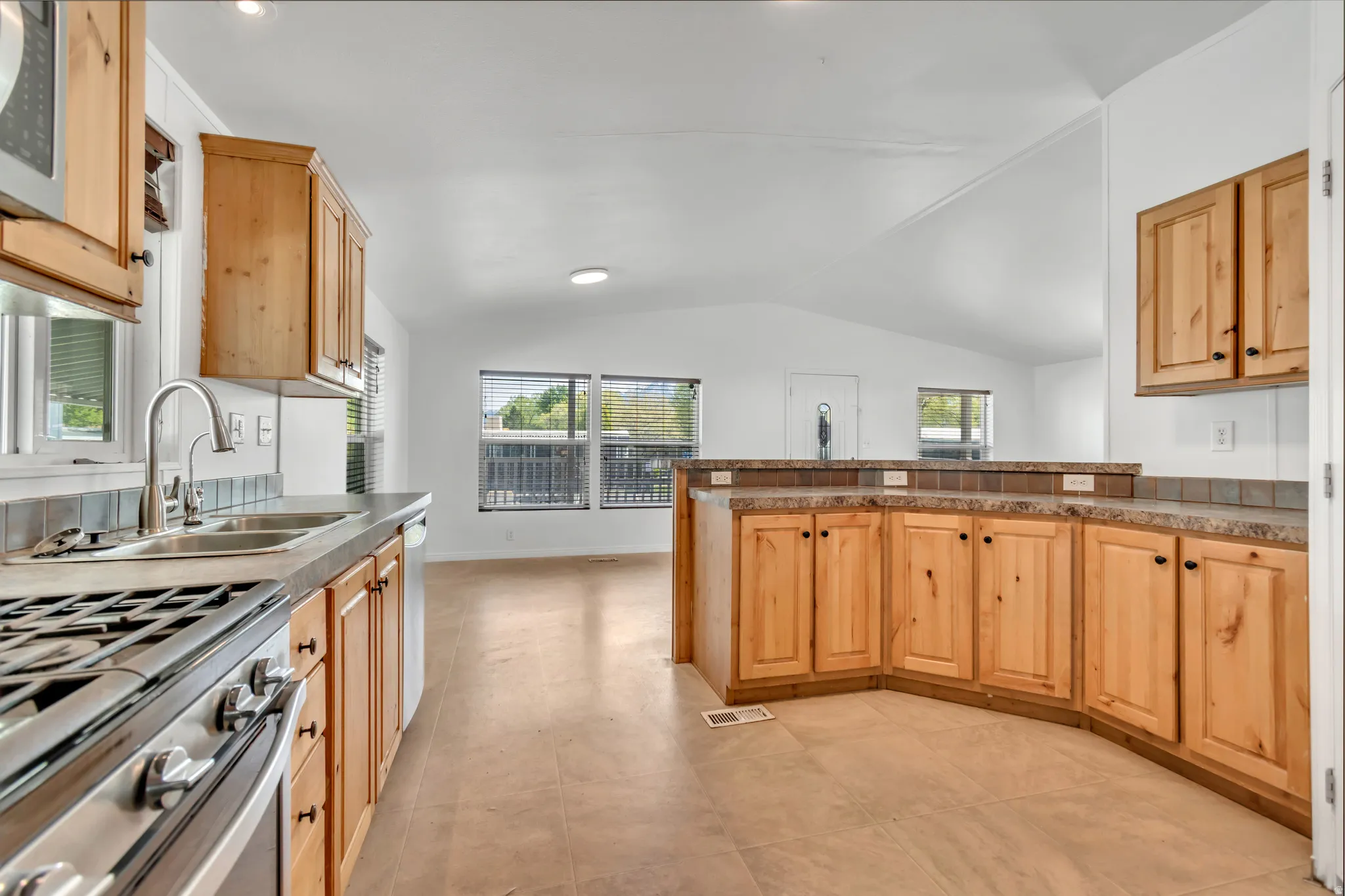 Kitchen featuring stainless steel gas stove, light wood finish cabinetry, a peninsula, vaulted ceiling, and dark countertops