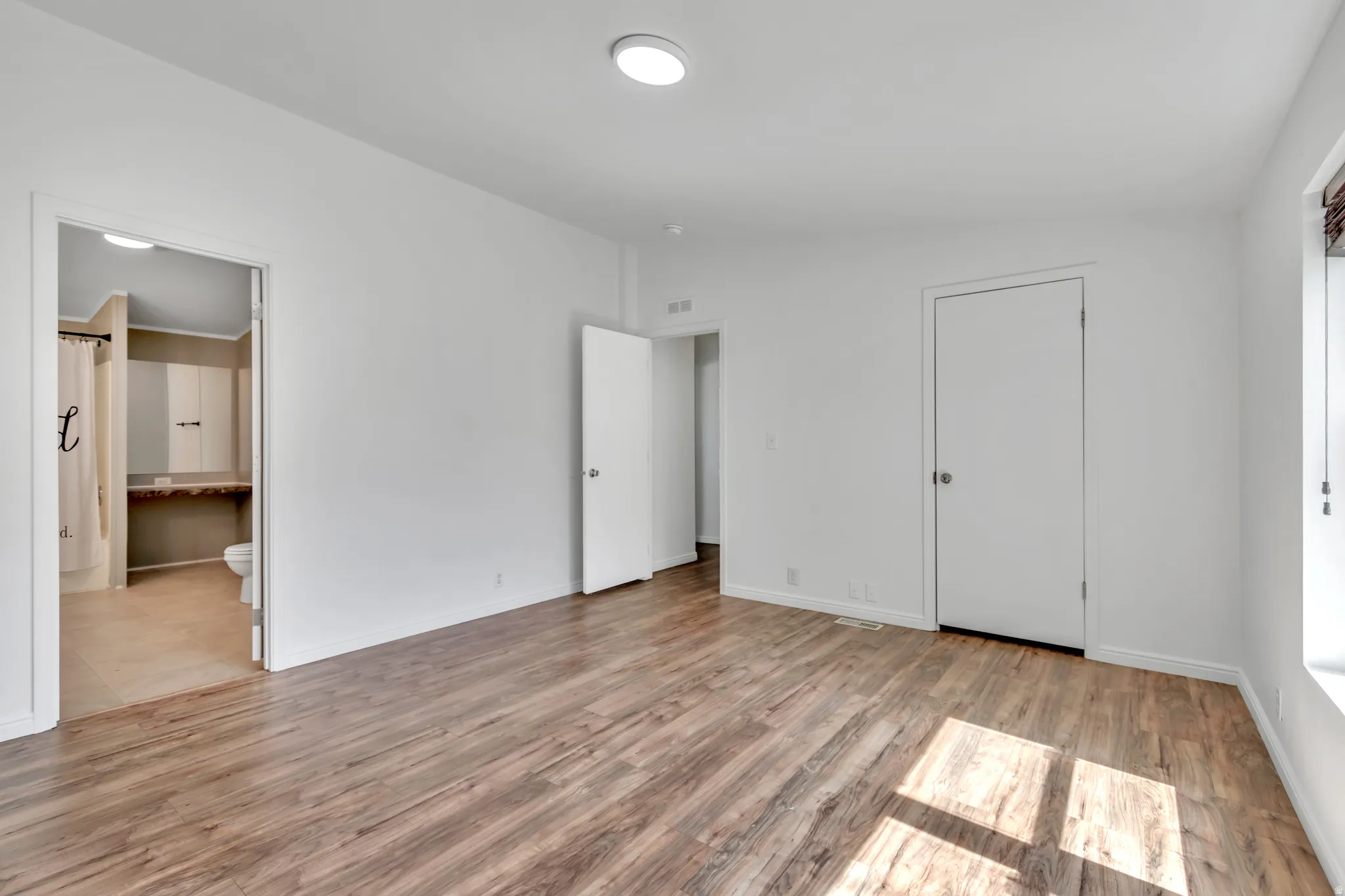 Unfurnished bedroom with light wood finished floors and connected bathroom
