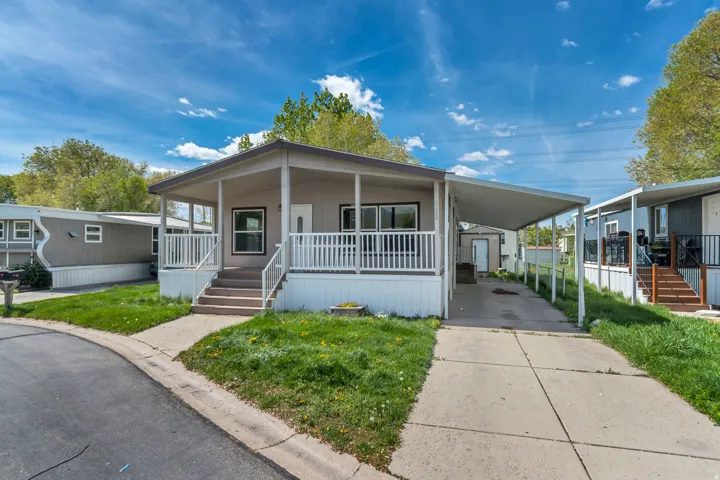 Manufactured / mobile home featuring a carport, a porch, a front lawn, and driveway