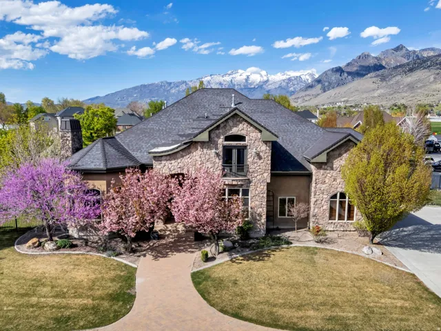 Front view of a 7,265 sq ft stucco and stone estate featuring a circular driveway, nestled in a quiet Pleasant Grove neighborhood with beautiful mountain views near Mount Timpanogos Temple.