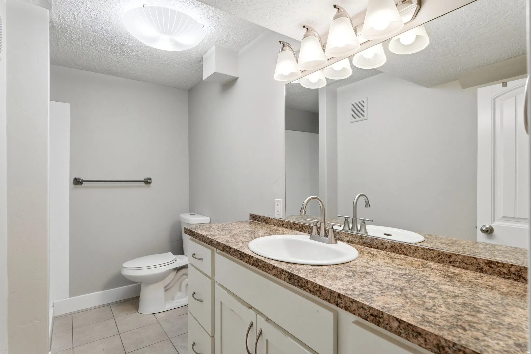 Full bath with vanity, a textured ceiling, and light tile patterned floors