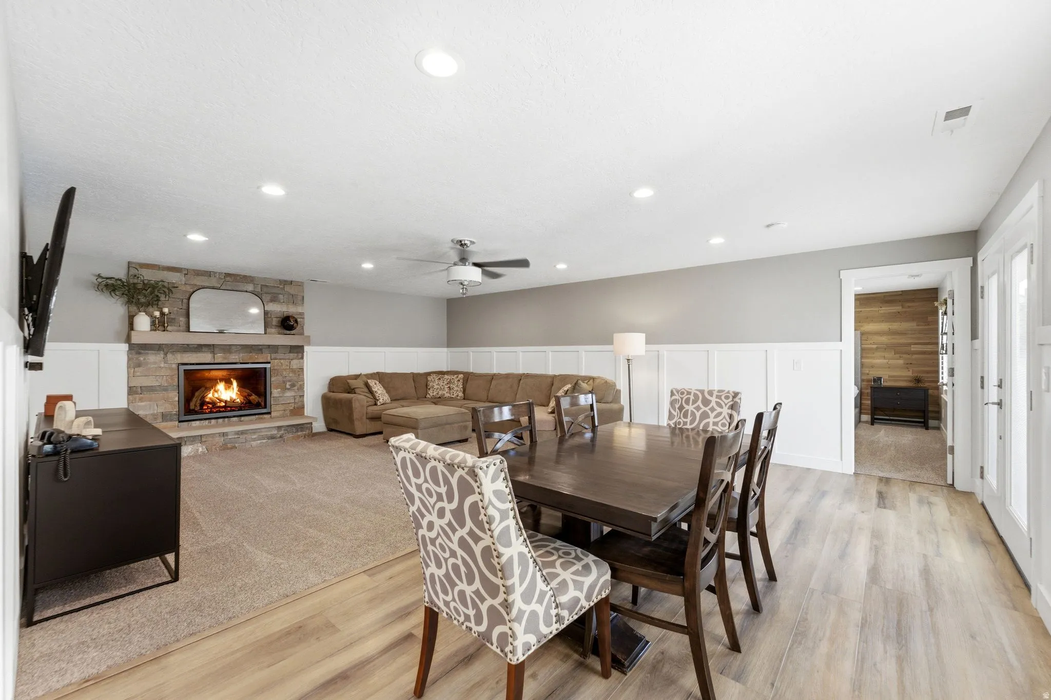 Dining space featuring a wainscoted wall, light wood-style flooring, a decorative wall, a stone fireplace, and a ceiling fan