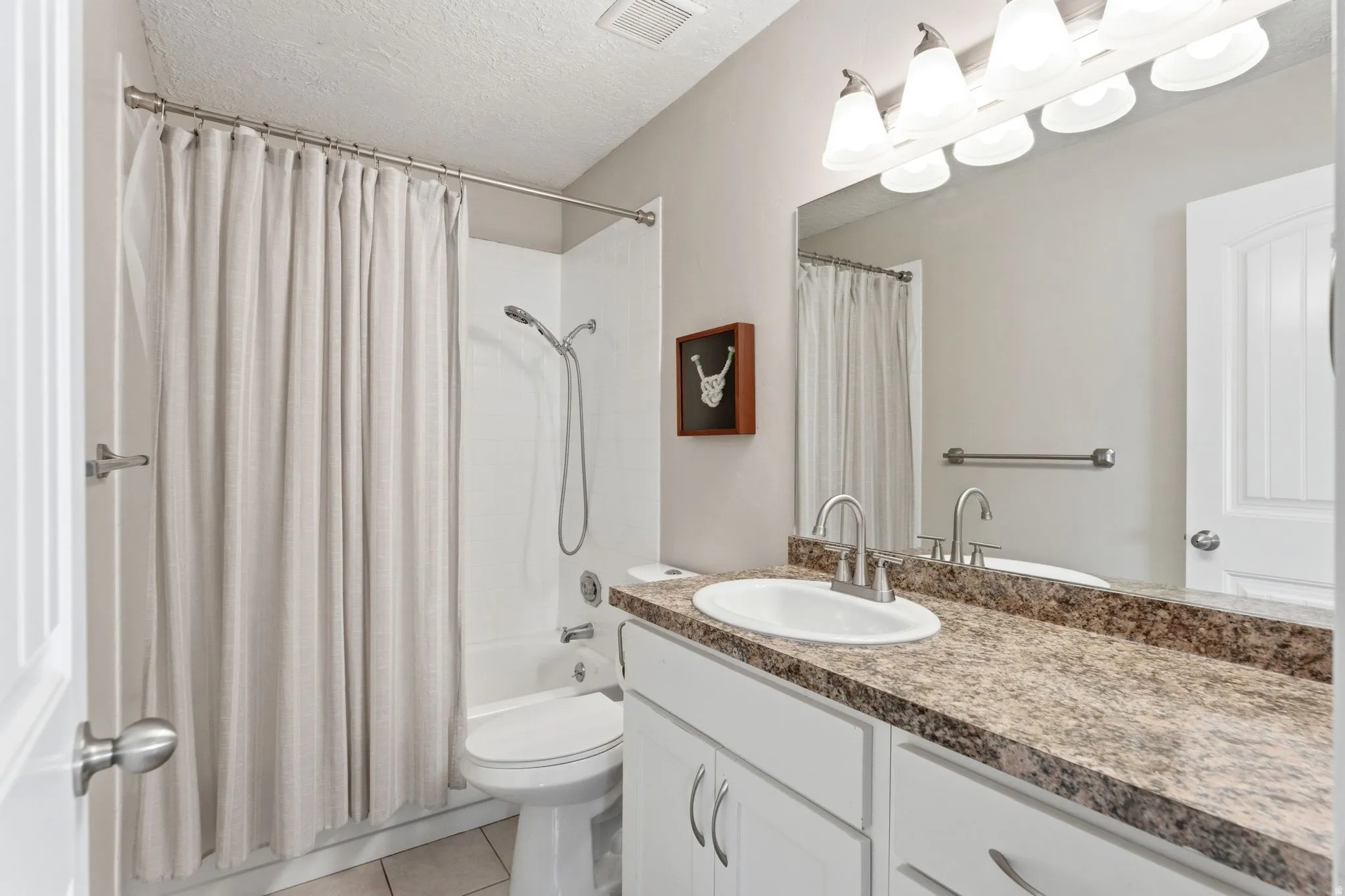 Bathroom with vanity, a textured ceiling, light tile patterned floors, and shower / bath combo
