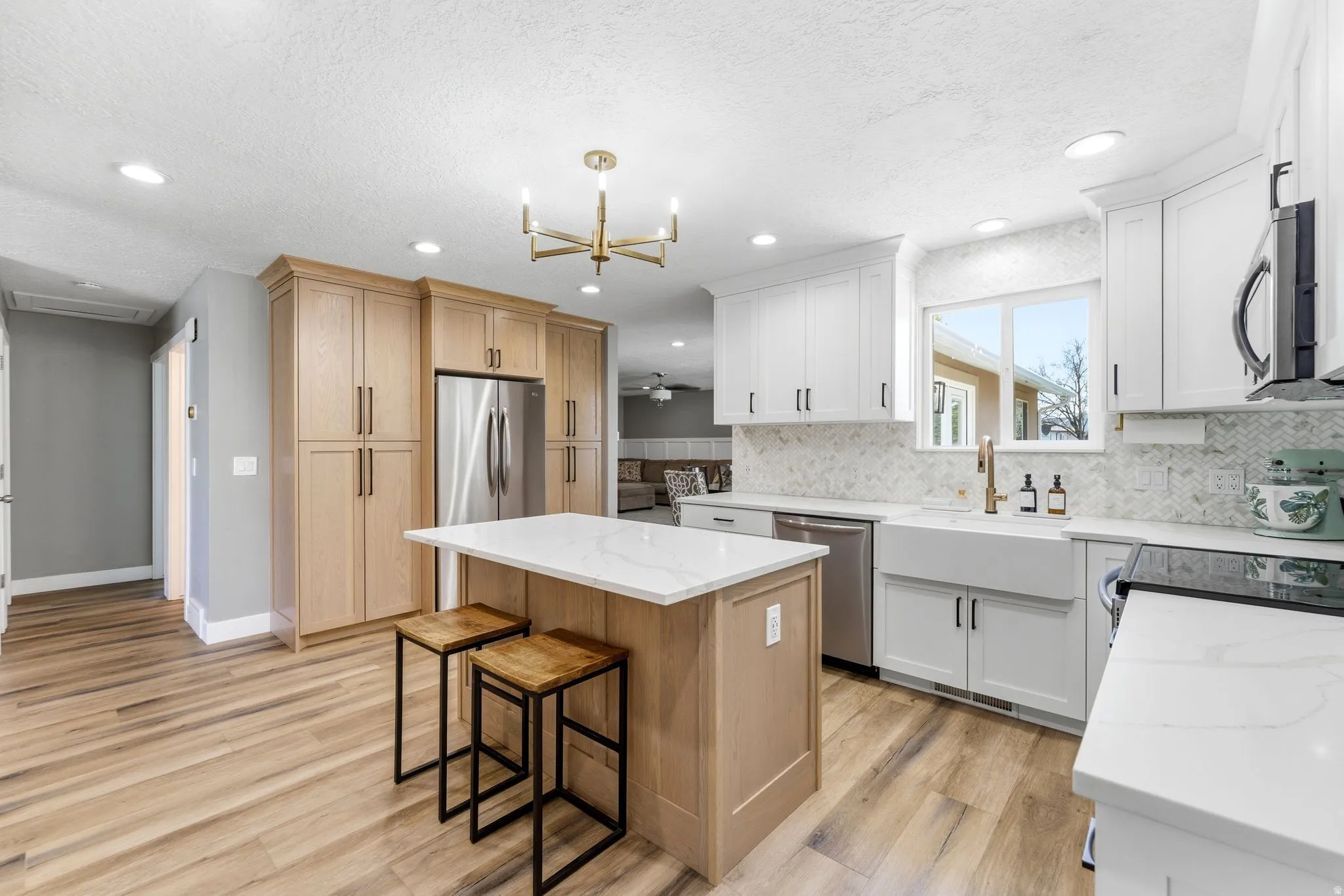 Dual tone kitchen featuring light stone countertops, light wood-style floors, a center island, stainless steel appliances, and a breakfast bar area