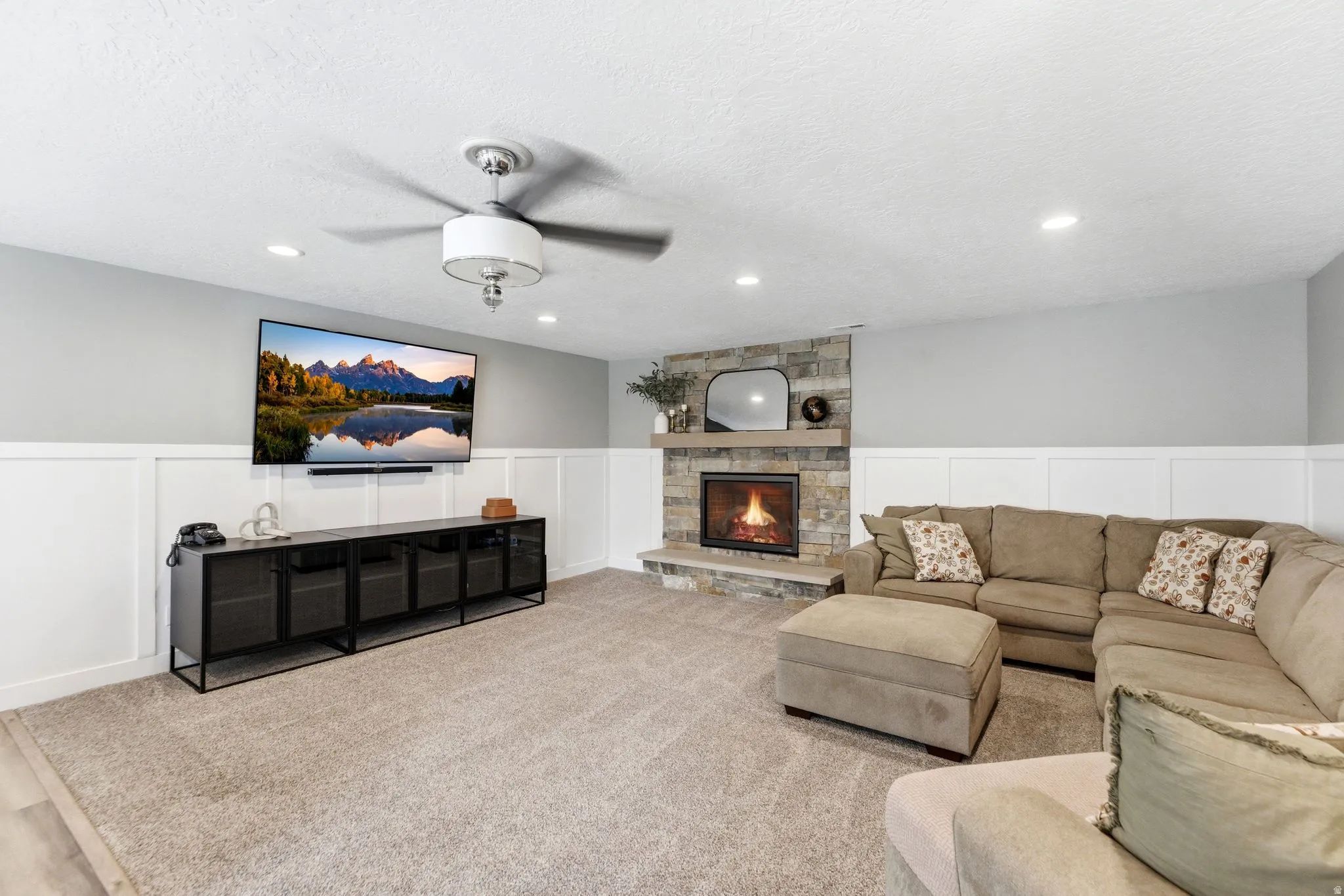 Living room with a decorative wall, wainscoting, a fireplace, ceiling fan, and carpet