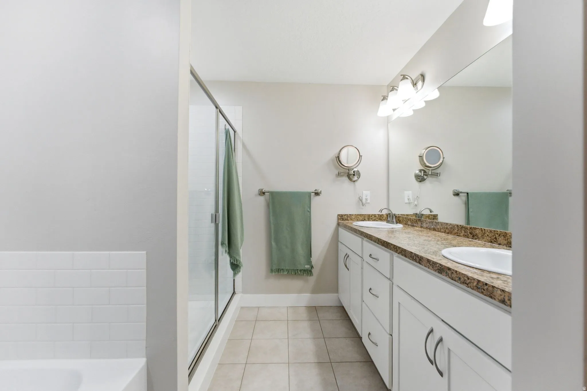 Full bathroom featuring double vanity, light tile patterned flooring, a garden tub, and a shower stall