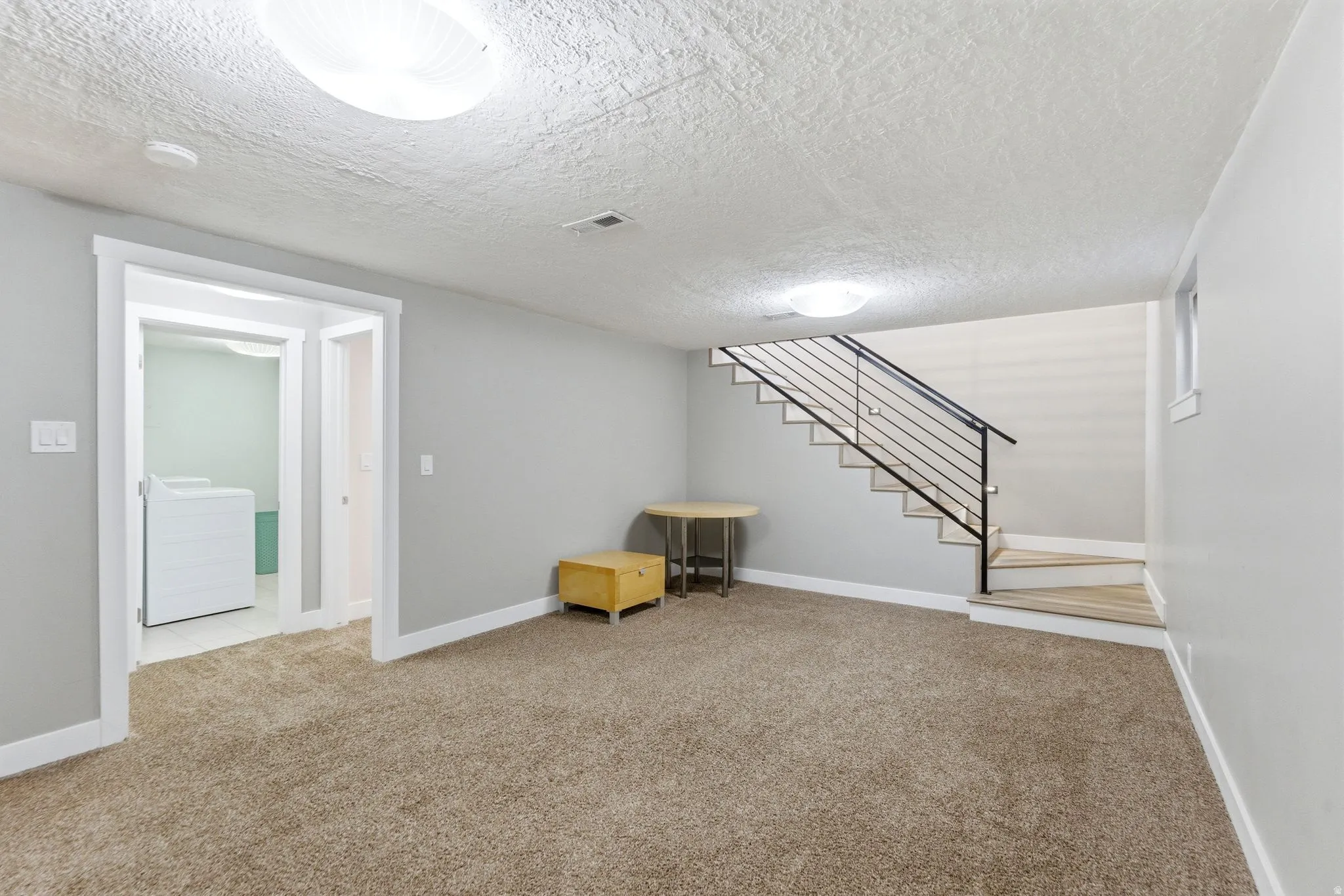 Finished basement featuring a textured ceiling, light colored carpet, and washing machine and clothes dryer