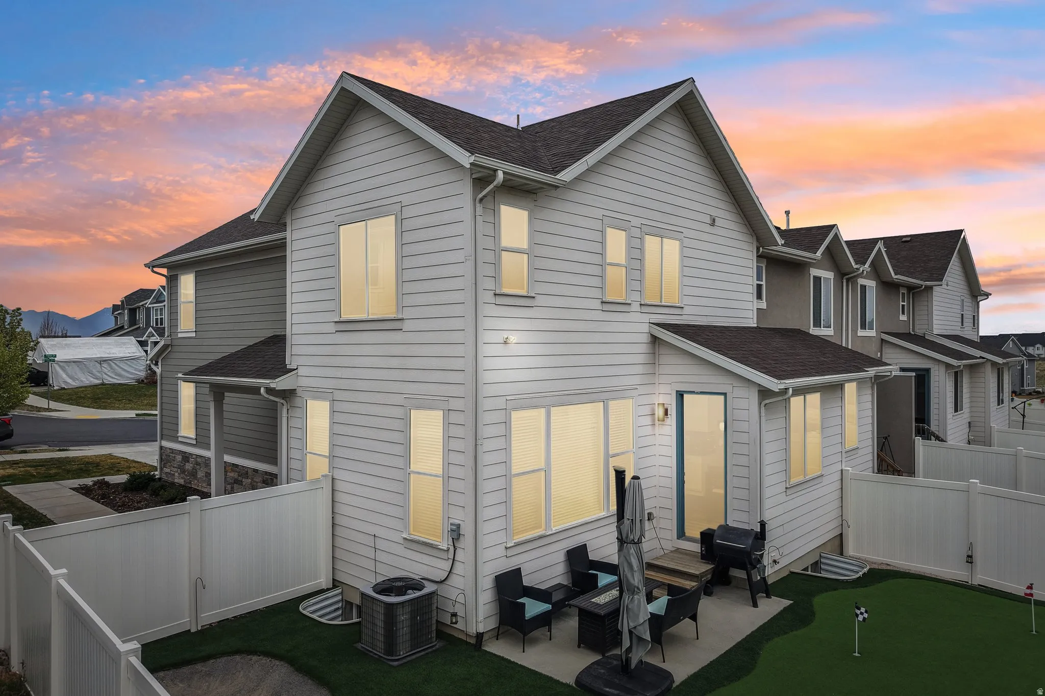 Back of property at dusk with roof with shingles, a fenced backyard, a putting area, and outdoor furniture