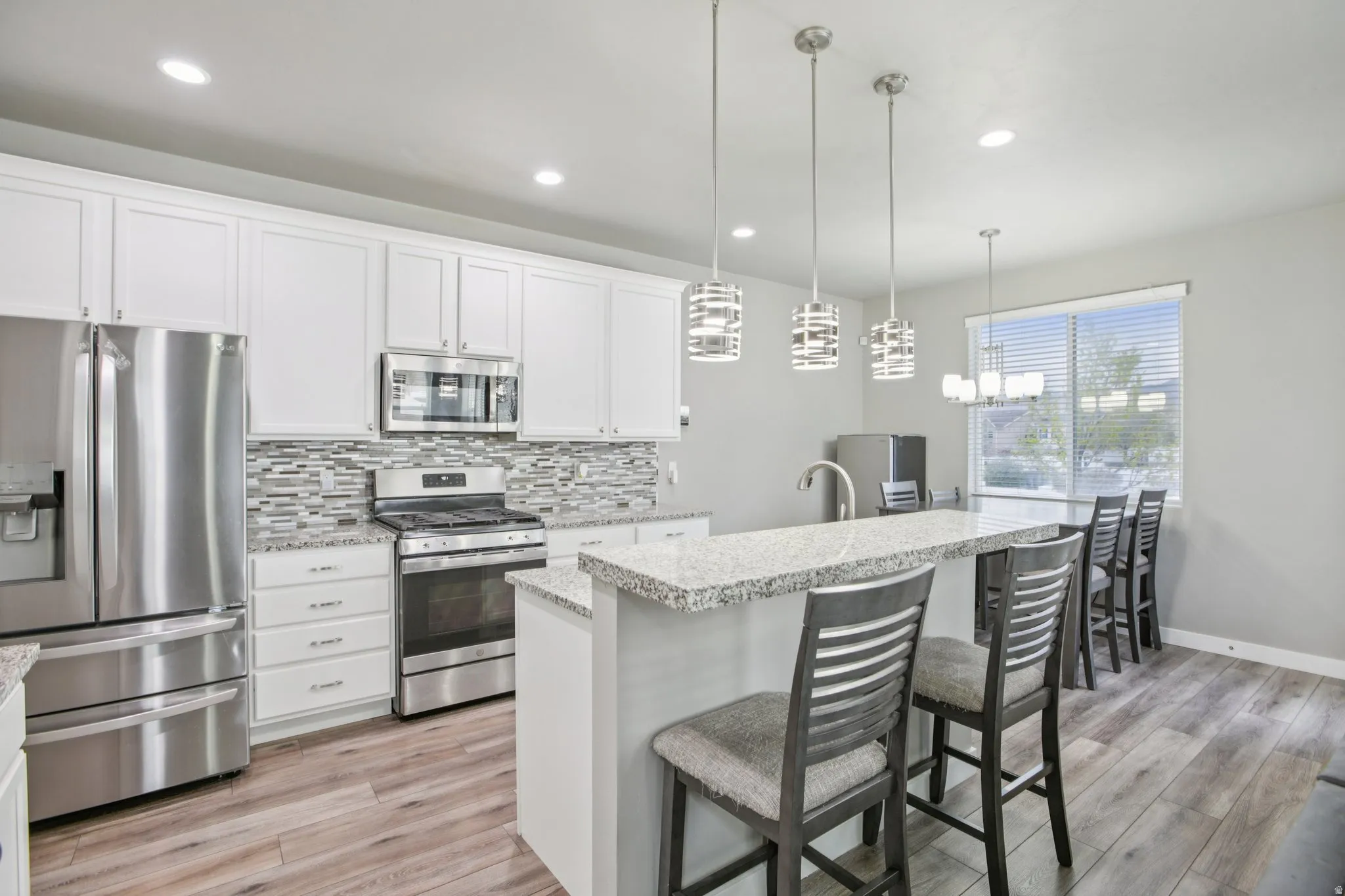 Kitchen featuring stainless steel appliances, decorative backsplash, white cabinets, light wood-style flooring, and hanging light fixtures