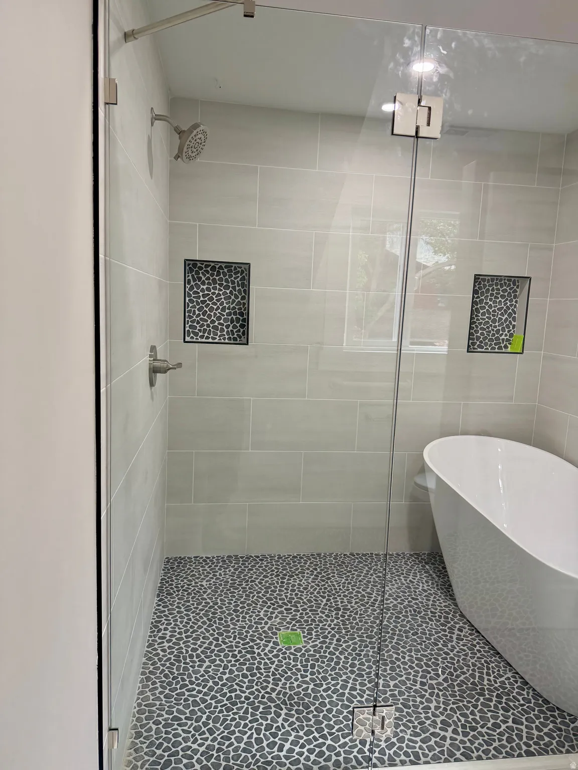 Glass-enclosed shower featuring a pebble-stone floor, light-toned rectangular wall tiles, and built-in shower niches
