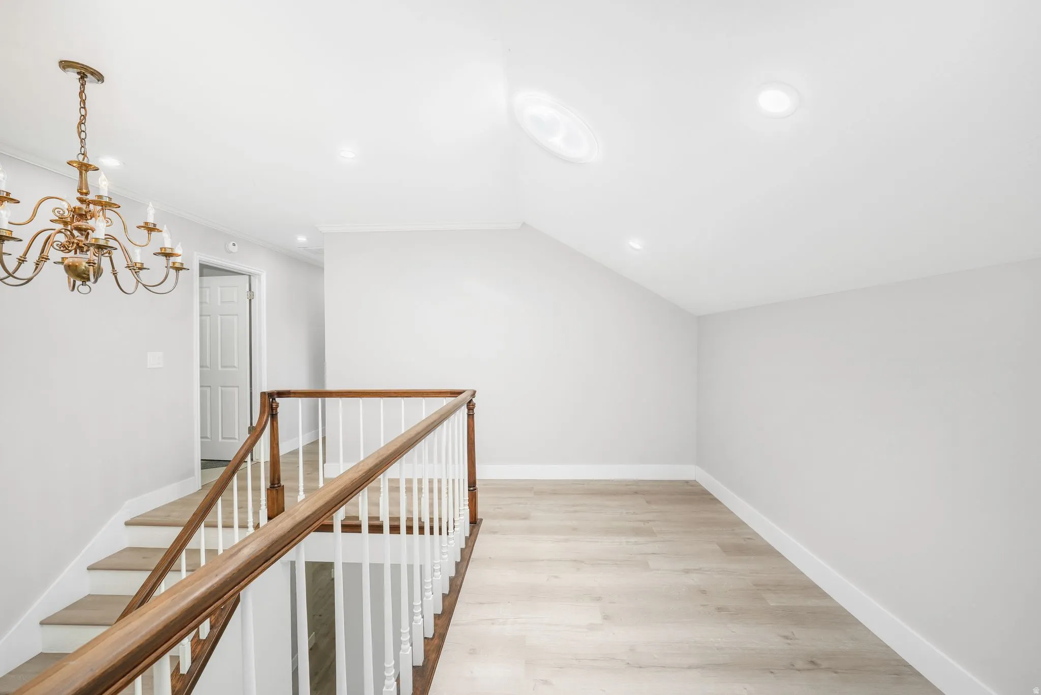 Hallway featuring light wood-type flooring, vaulted ceiling, an upstairs landing, and hanging lights
