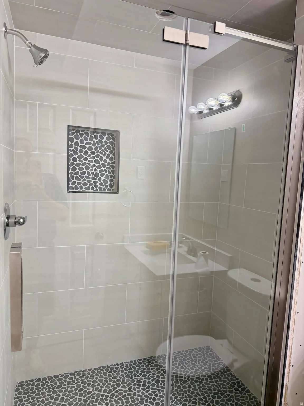 Glass-enclosed shower featuring a pebble-stone floor and a tile niche with decorative stone inlay