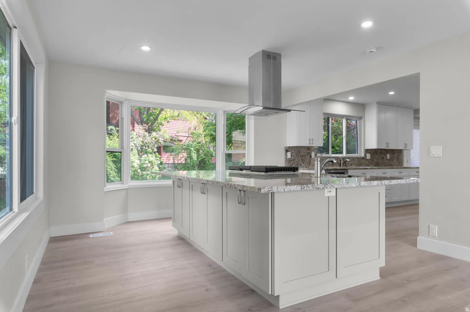 Kitchen featuring light stone counters, island exhaust hood, light wood-style floors, decorative backsplash, and recessed lighting